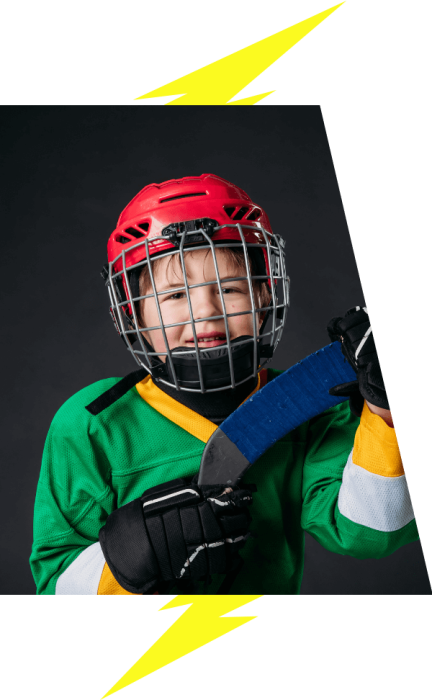 A child hockey player wears a green jersey and red helmets, holds hockey stick blade.